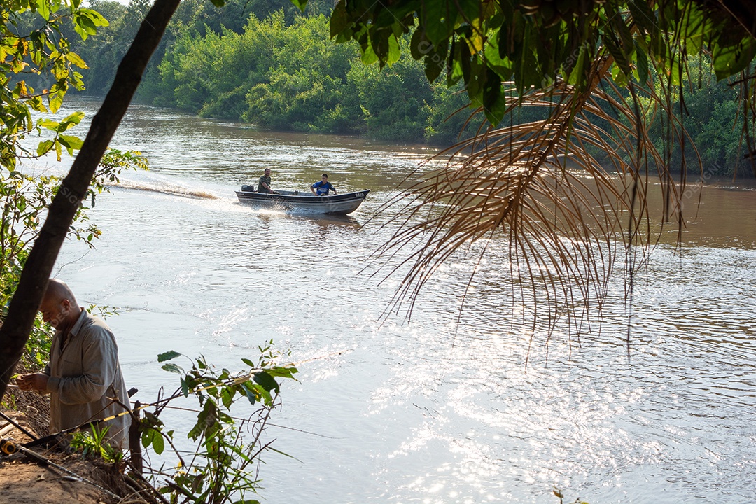 Mato grosso do sul / brasil - pescador, pescando no rio aquidauana no pantanal enquanto um barco com mais pescadores se aproxima