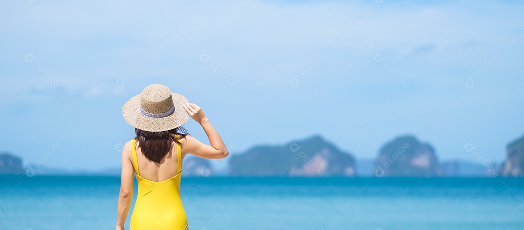 Turista de mulher de maiô amarelo e chapéu, feliz viajante tomando sol na praia do paraíso nas ilhas. destino, desejo de viajar, verão tropical, férias e conceito de férias