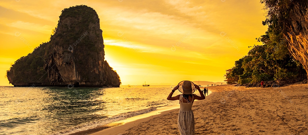 Mulher turista de vestido branco e chapéu andando na praia da caverna de Phra nang ao pôr do sol, Railay, Krabi, Tailândia. férias, viagens, verão, Wanderlust e conceito de férias