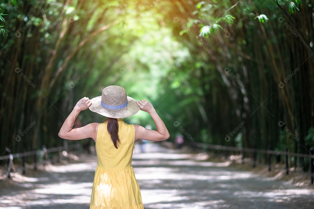 Mulher asiática de vestido amarelo e chapéu viajando em bambu verde Tu