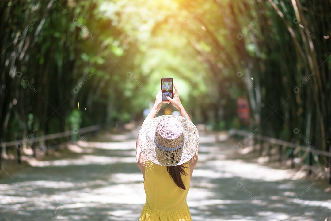 Mulher asiática de vestido amarelo e chapéu viajando em bambu verde
