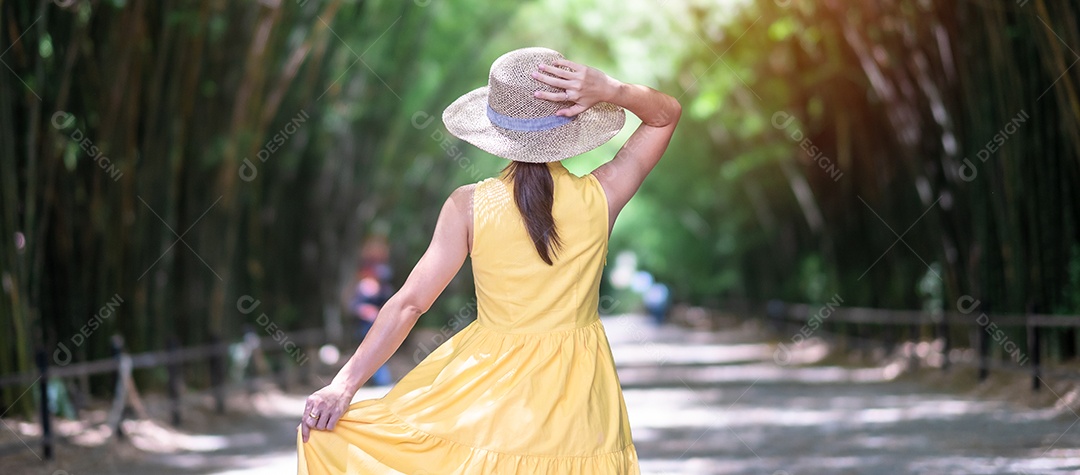 Mulher asiática de vestido amarelo e chapéu viajando em bambu verd