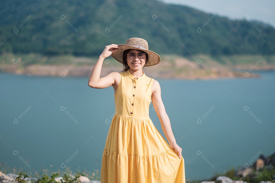 Mulher asiática de vestido amarelo e chapéu viajando ao ar livre, viajante feliz olhando para a represa de Khun dan Prakarnchon. Marco e popular para atrações turísticas em Nakhon Nayok, Tailândia