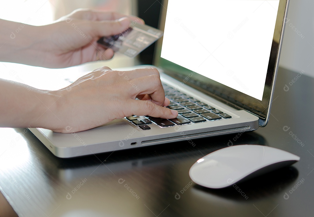Mãos segurando um cartão de crédito e usando o computador portátil.