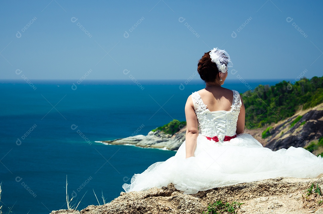 Noiva sentada em uma pedra à beira-mar.