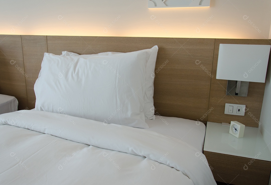 Interior do quarto com almofadas e candeeiro de leitura na cabeceira.