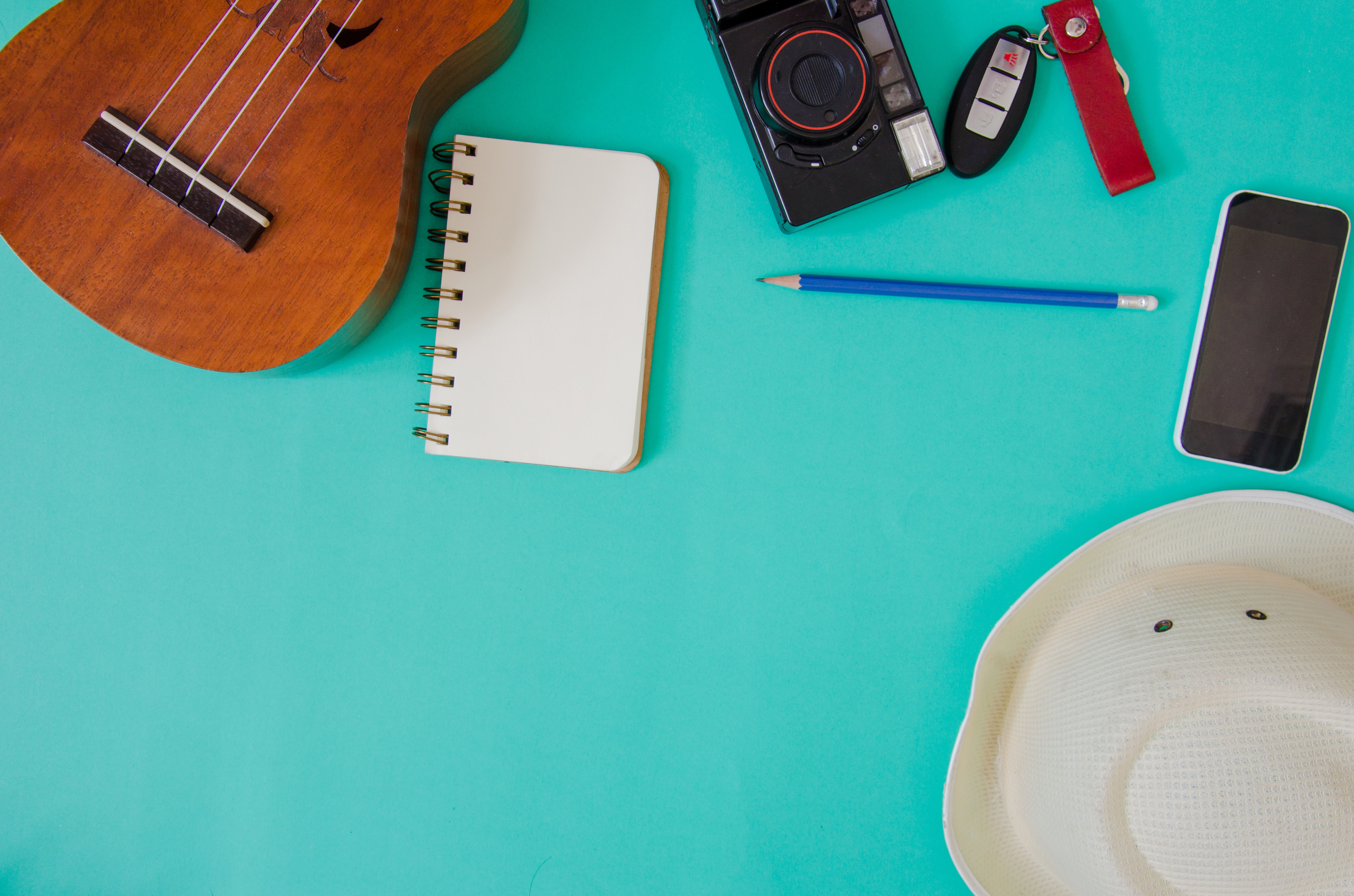 Acessórios de viajante. Chapéu, ukulele, lápis e cadernos. e telefone no fundo verde.