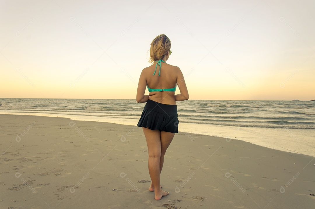 Mulher vestindo biquíni em pé na praia.