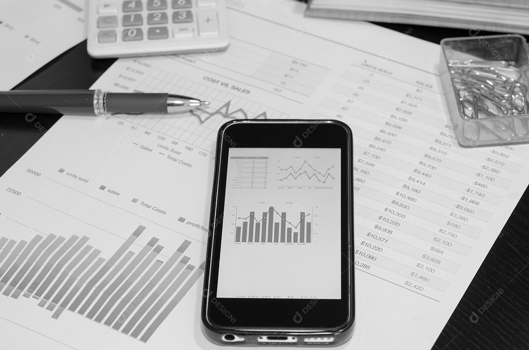 Telefone inteligente e gráfico em cima da mesa. Foto preto e branco.