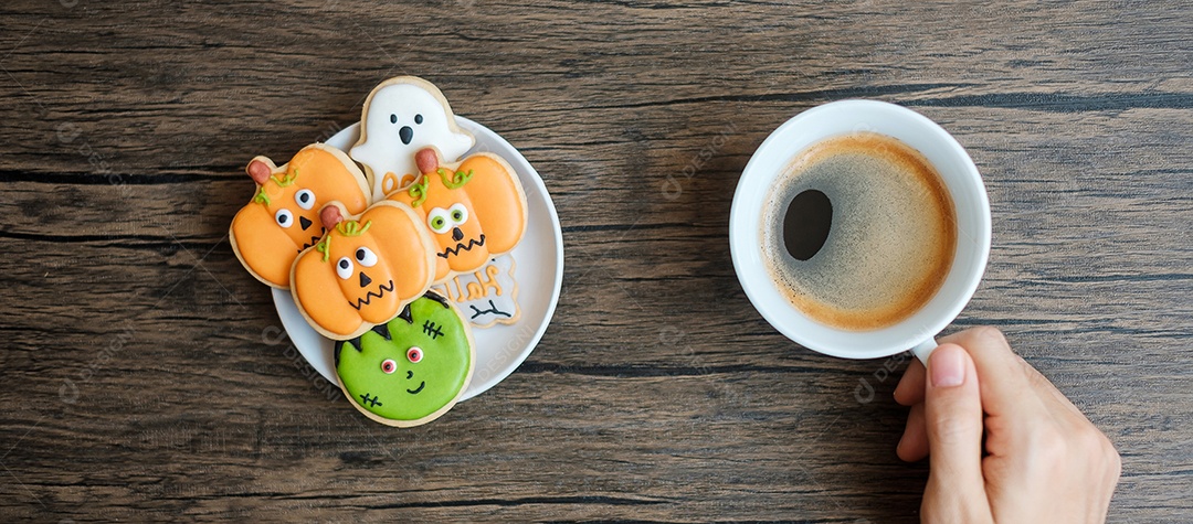 mão segurando a xícara de café durante comer biscoitos engraçados de Halloween.