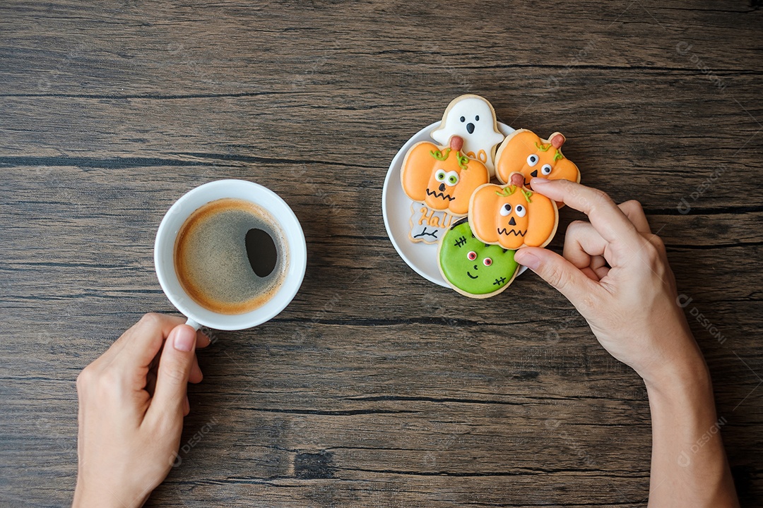 mão segurando a xícara de café durante comer biscoitos engraçados de Halloween