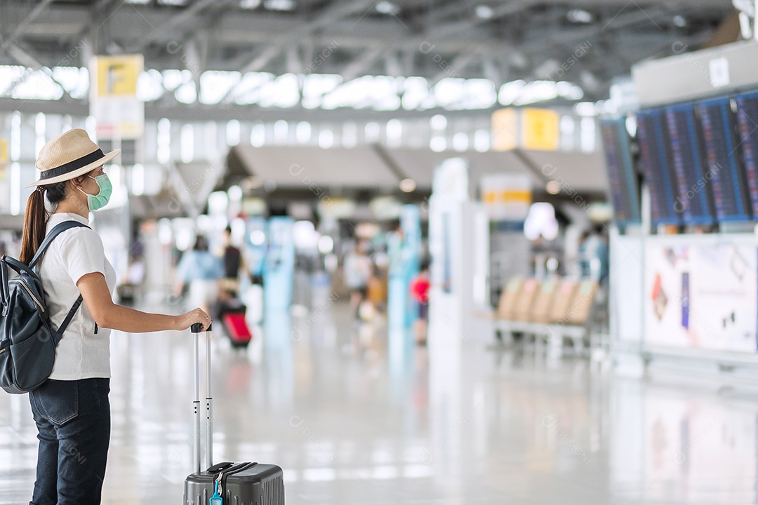 Jovem mulher usando máscara facial com bagagem andando no aeroporto