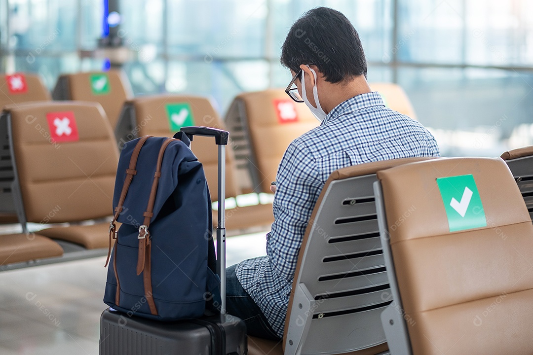 Jovem homem usa máscara facial sentado na cadeira no terminal do aeroporto