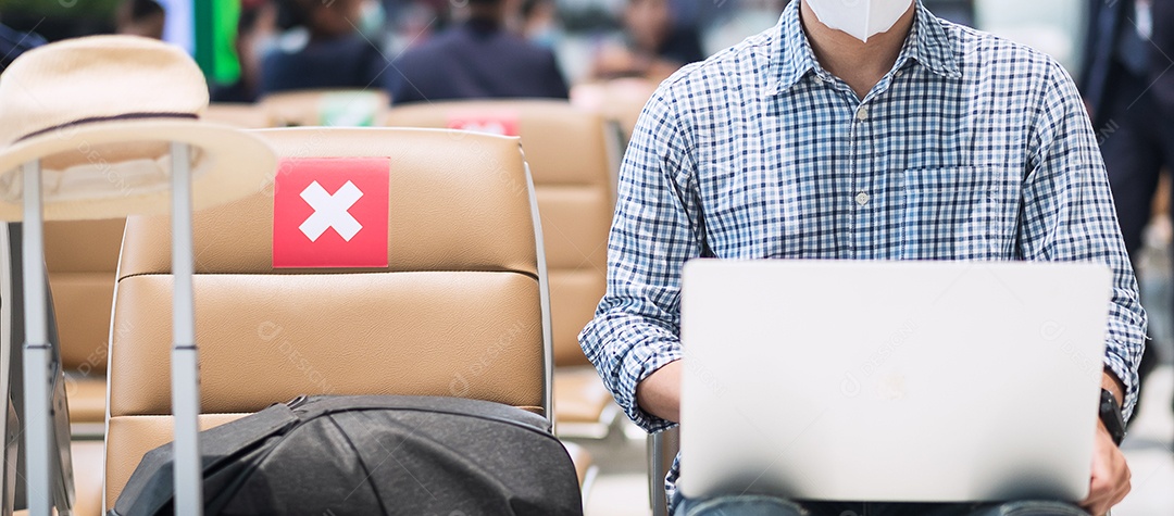 Jovem macho usando máscara facial e usando laptop de computador no aeroporto