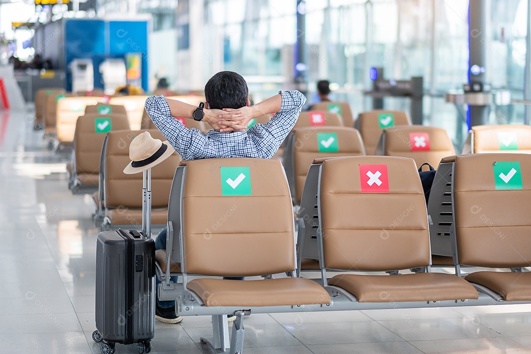 Jovem homem usa máscara facial sentado na cadeira no terminal do aeroporto
