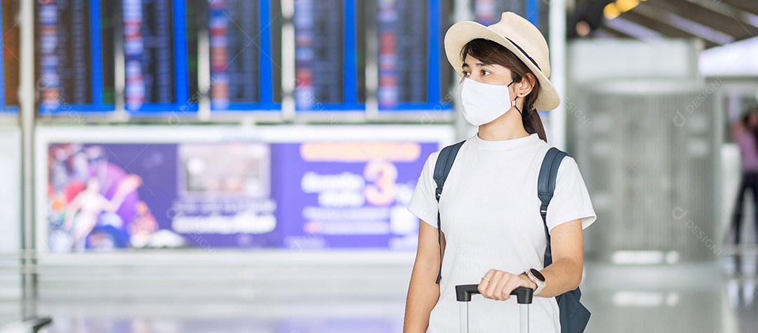 Young woman wearing face mask with luggage checking flight time