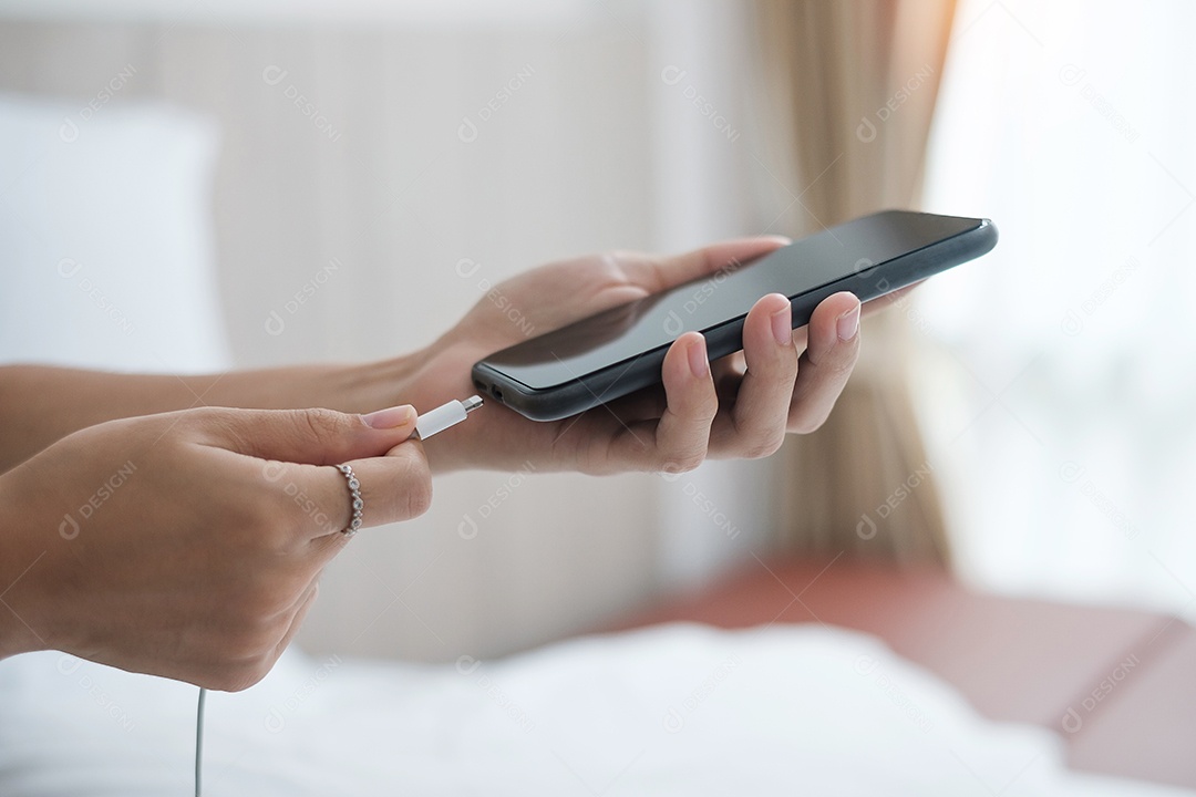 Mãos de mulher carregando bateria no celular inteligente no quarto