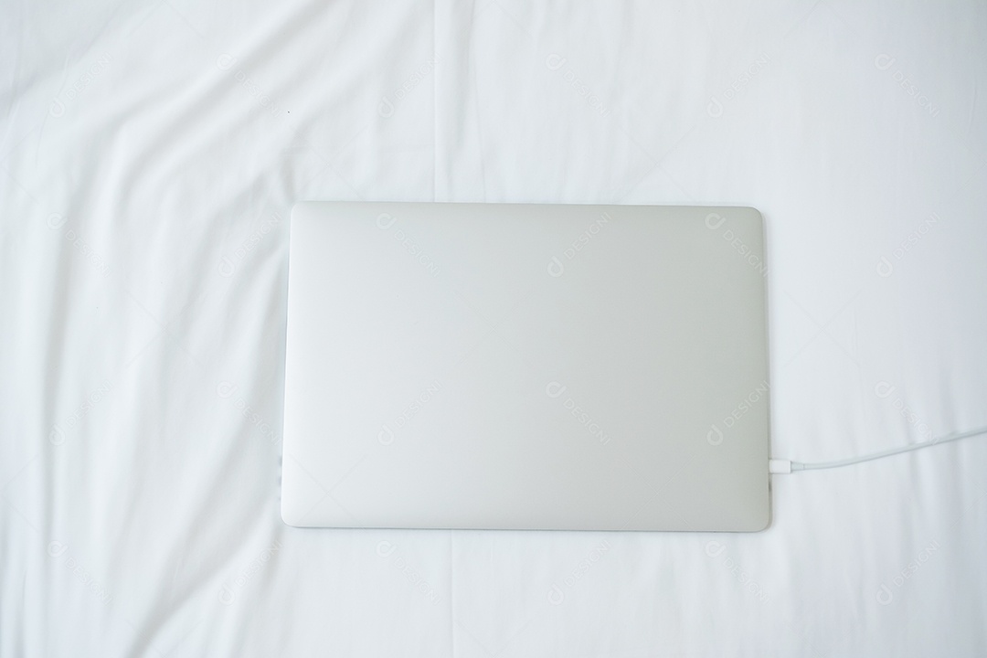 Computador portátil carregando bateria na cama no quarto em casa.