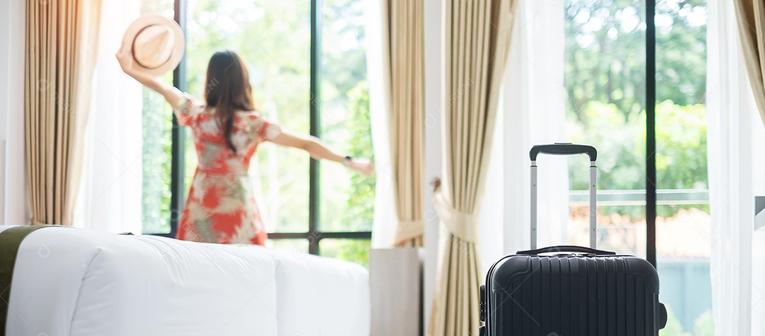 Bagagem no quarto de hotel moderno com fêmea adulta jovem feliz relaxa