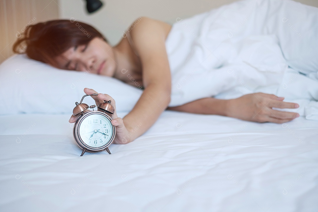 despertador e mão de mulher asiática param o tempo na cama enquanto dorme