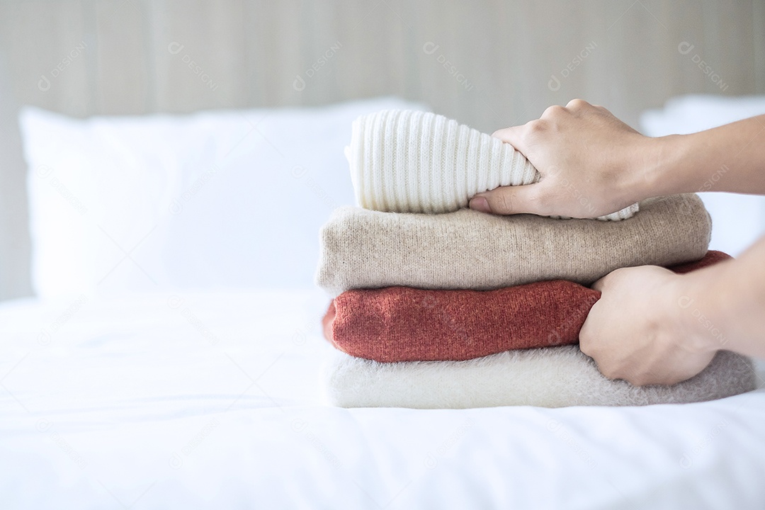 As mãos da mulher organizam camisolas de lã bege na cama no hotel de luxo