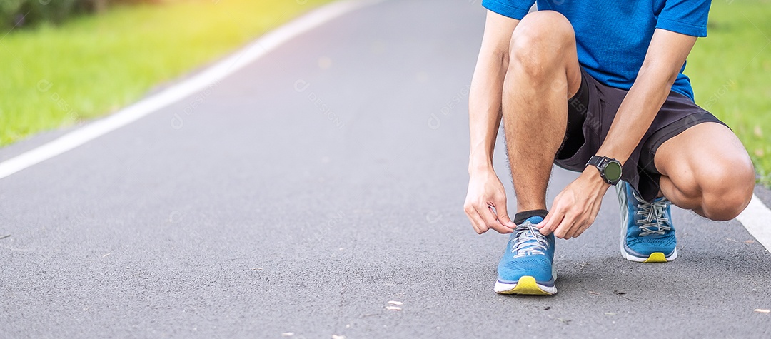 Macho adulto jovem em roupas esportivas amarrando cadarço no parque ao ar livre