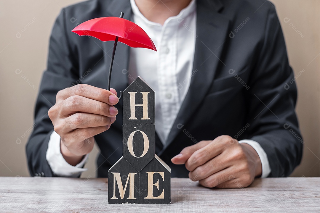 Mão de empresário segurando um guarda-chuva vermelho modelo de casa de madeira em