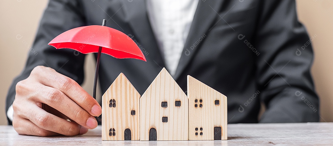 Mão de empresário segurando um guarda-chuva vermelho modelo de casa de madeira