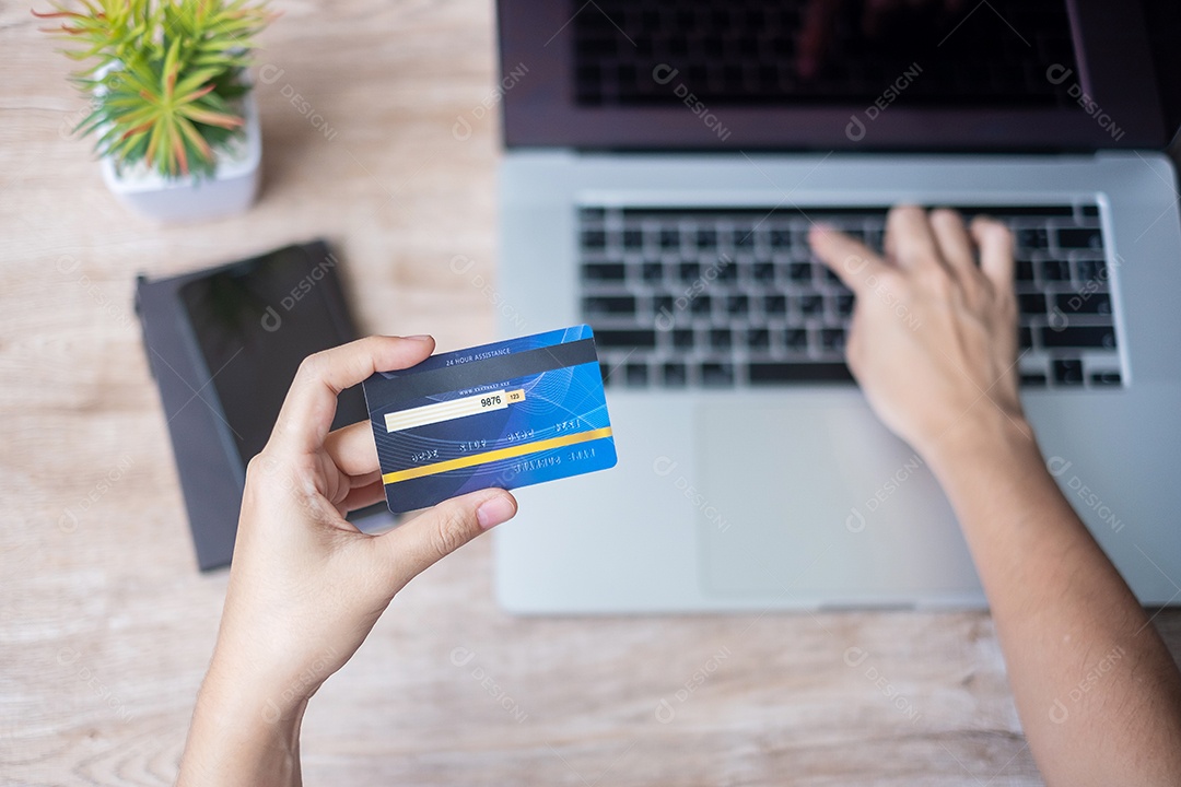 mulher vestindo suéter segurando cartão de crédito e usando laptop