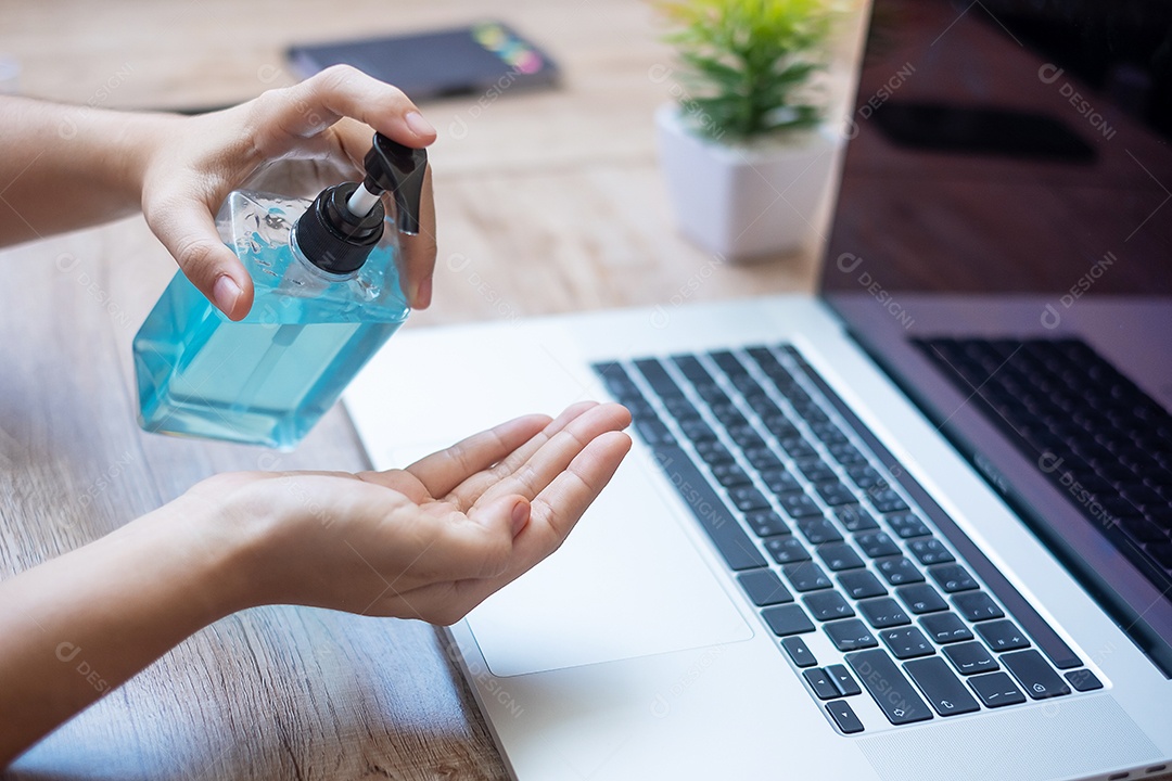 Mulher limpando as mãos por desinfetante de gel de álcool sobre laptop no wor
