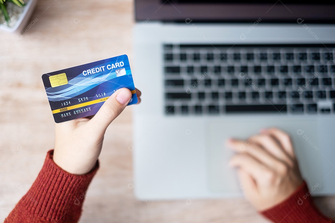 mulher vestindo suéter segurando cartão de crédito e usando laptop