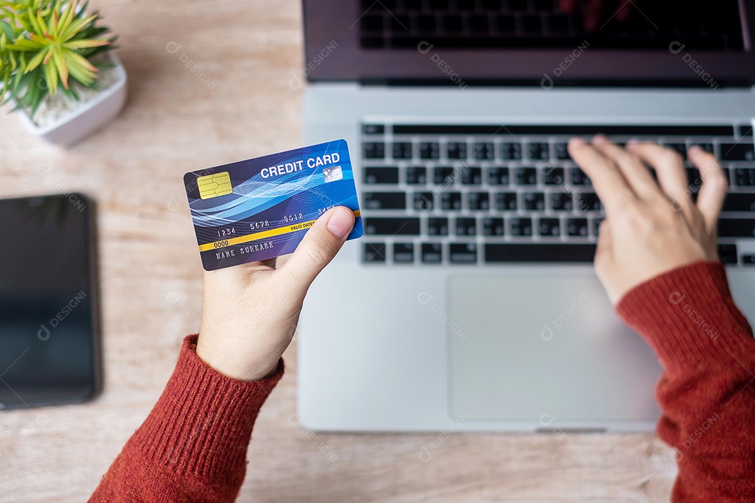 mulher vestindo suéter segurando cartão de crédito e usando laptop