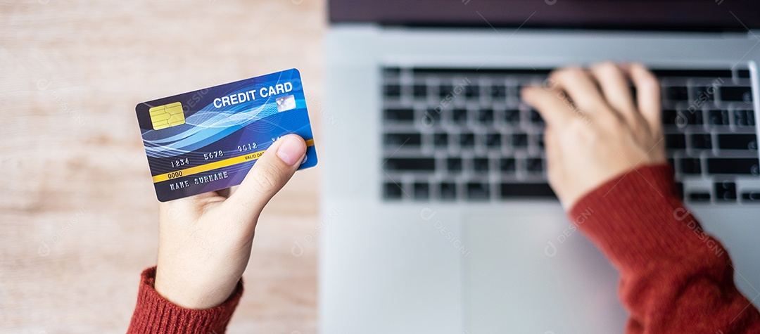 mulher vestindo suéter segurando cartão de crédito e usando laptop