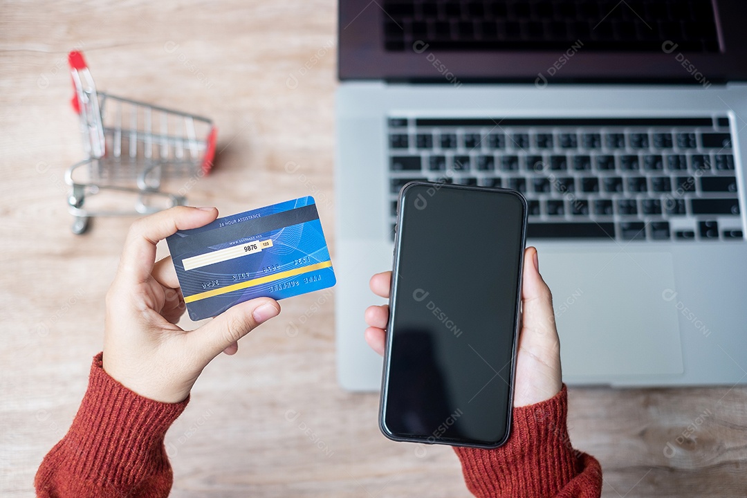 mulher vestindo suéter segurando cartão de crédito e usando celular