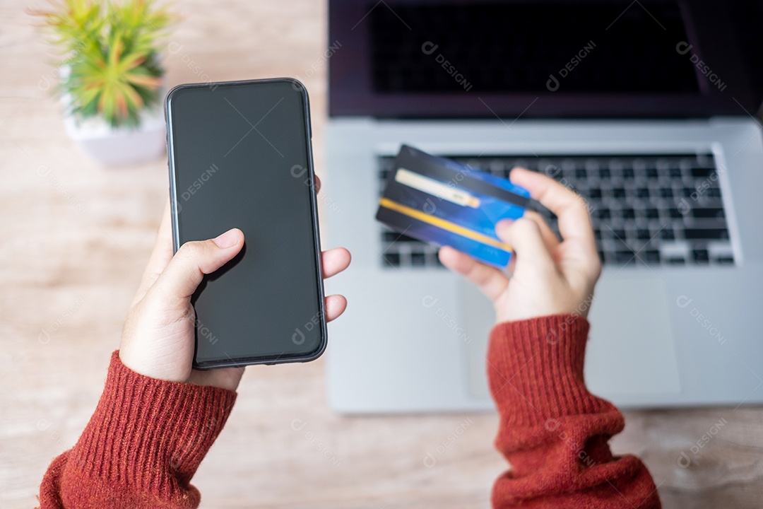 mão de mulher segurando o cartão de crédito com o uso de smartphone e laptop