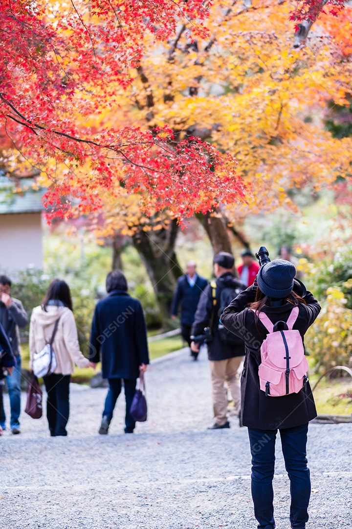 turista de mulher tirando foto de folhas coloridas pela câmera em Tenryuji