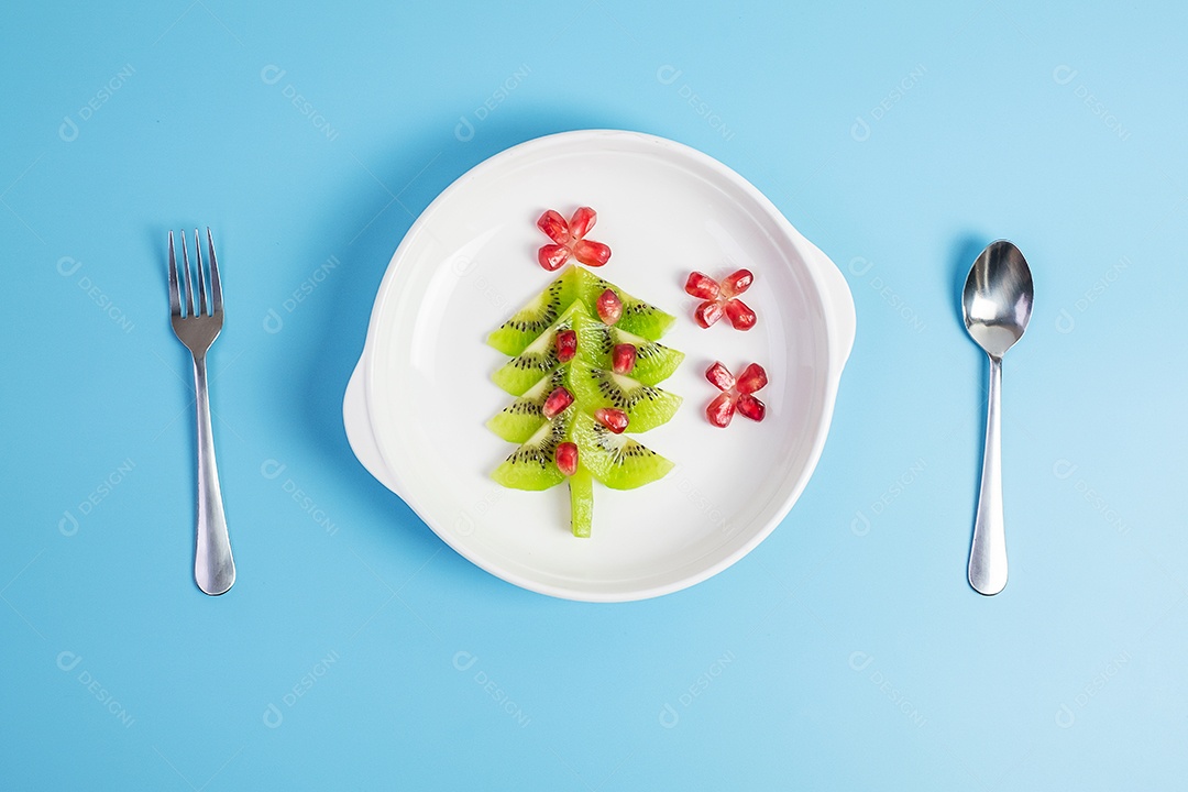 Árvore de Natal de frutas; Semente de kiwi e romã com garfo e faca sobre fundo azul. Feliz natal e feliz festa de ano novo, novo você, comida saudável e vegetariana