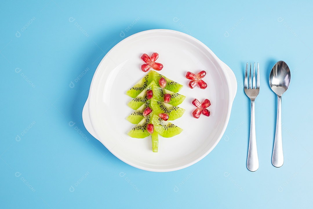 Árvore de Natal de frutas; Semente de kiwi e romã com garfo e faca sobre fundo azul. Feliz natal e feliz festa de ano novo, novo você, comida saudável e vegetariana