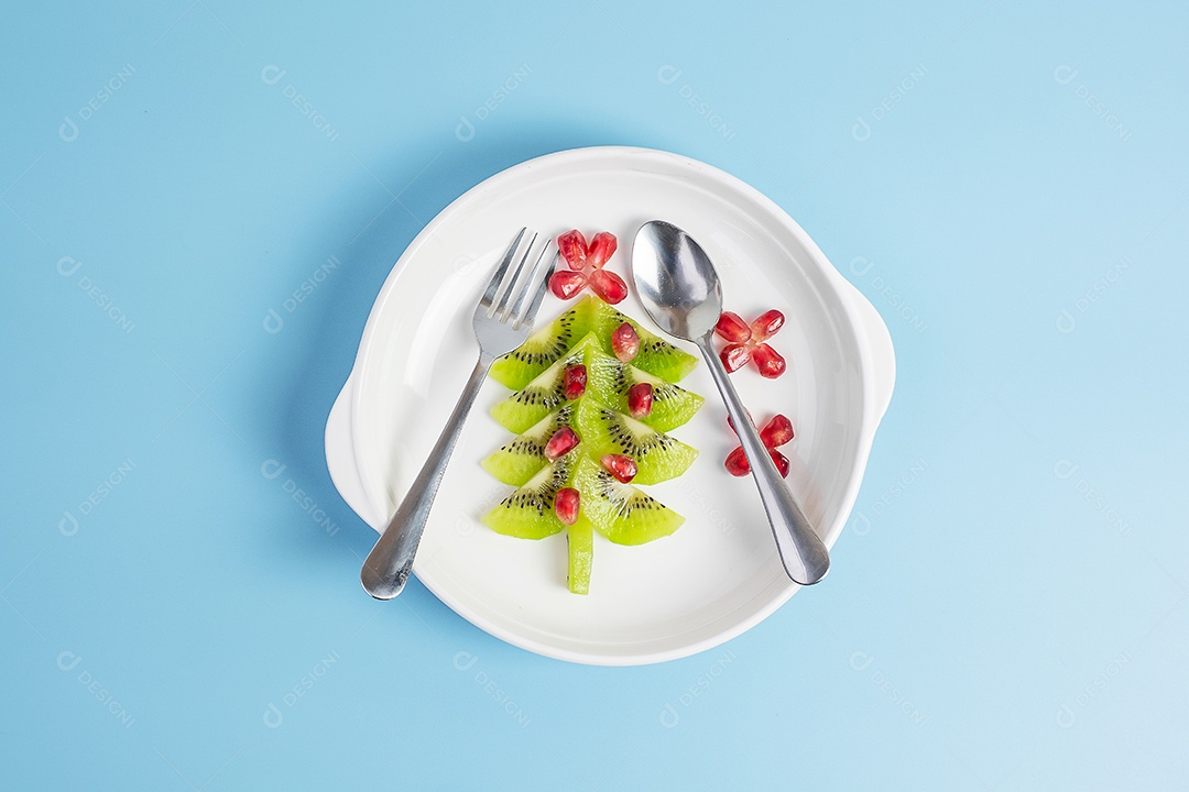 Árvore de Natal de frutas; Semente de kiwi e romã com garfo e faca sobre fundo azul. Feliz natal e feliz festa de ano novo, novo você, comida saudável e vegetariana