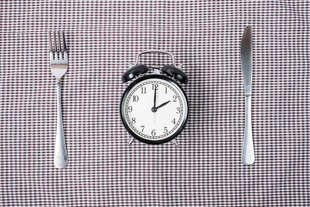 Vista superior despertador com faca e garfo no fundo da toalha de mesa. Jejum intermitente, dieta cetogênica, perda de peso, plano de refeições e conceito de alimentação saudável