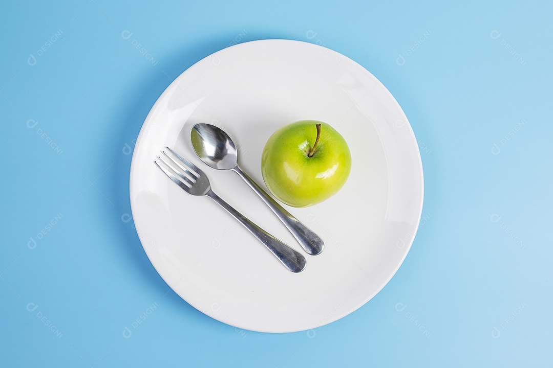 Colher e garfo de vista superior, maçã verde na placa cerâmica branca
