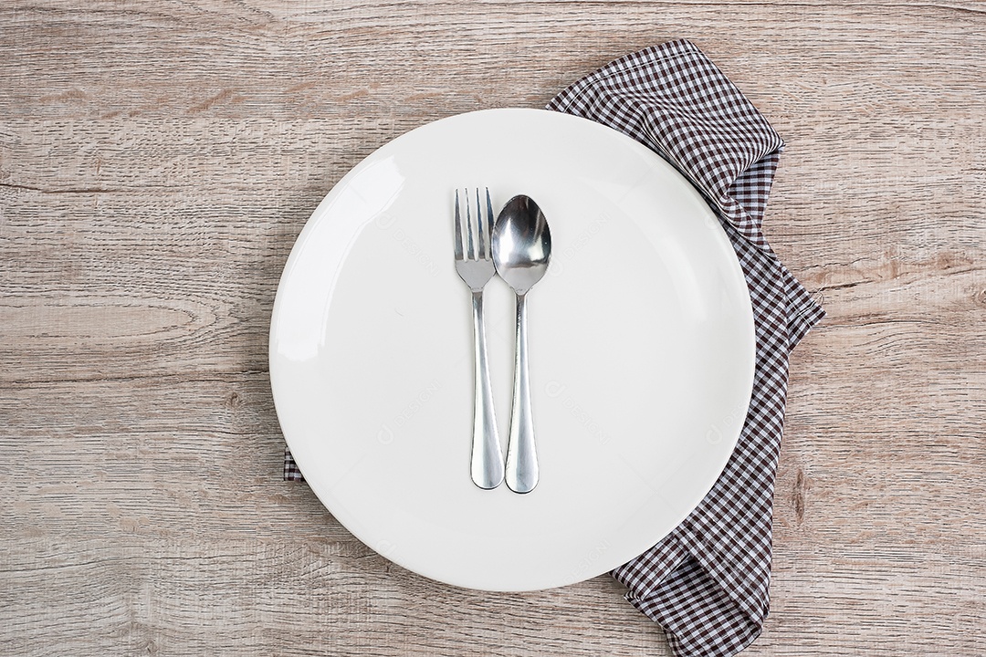 prato de cerâmica branco vazio com colher e garfo no fundo da mesa. conceito de jantar e utensílios de cozinha