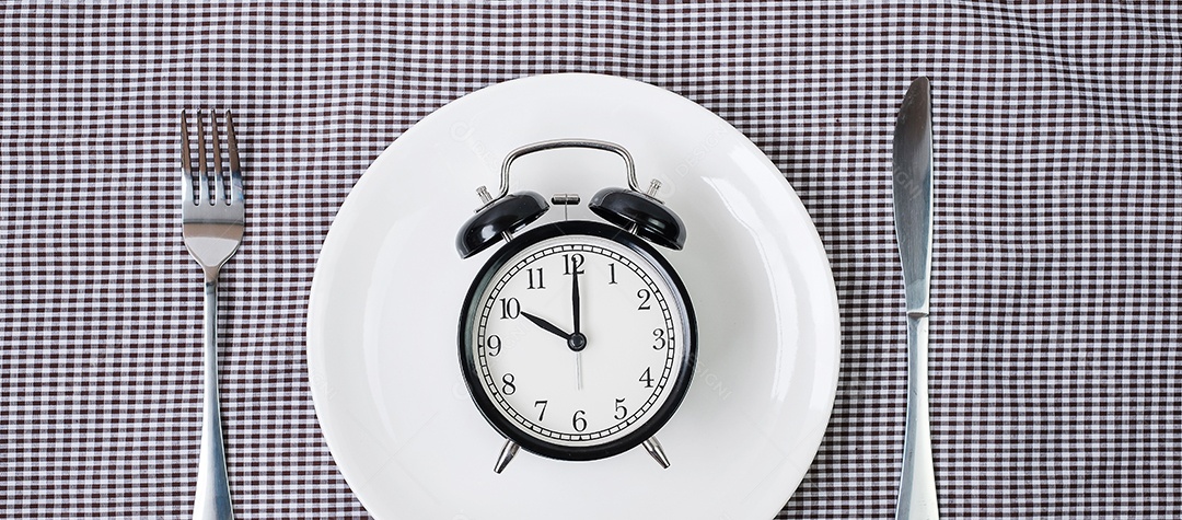 faca e garfo com despertador na chapa branca sobre fundo de toalha de mesa. Jejum intermitente, dieta cetogênica, perda de peso