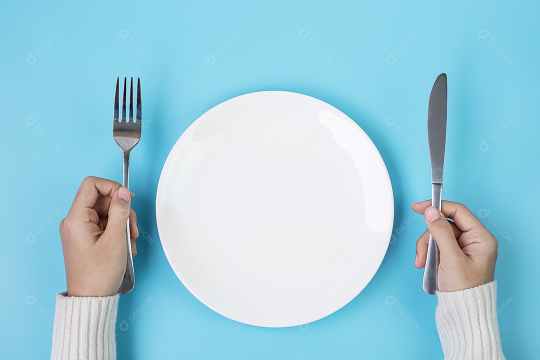 Mãos segurando faca e garfo acima da placa branca sobre fundo azul., dieta, perda de peso, jantar e conceito de utensílios de cozinha