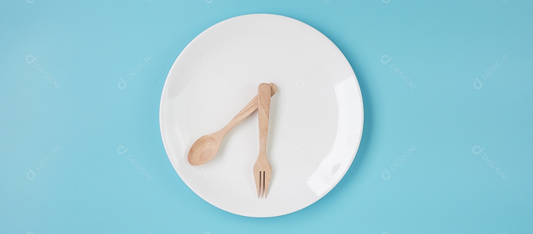 Vista superior placa cerâmica branca com faca, colher e garfo sobre fundo azul. Jejum intermitente, dieta cetogênica, perda de peso