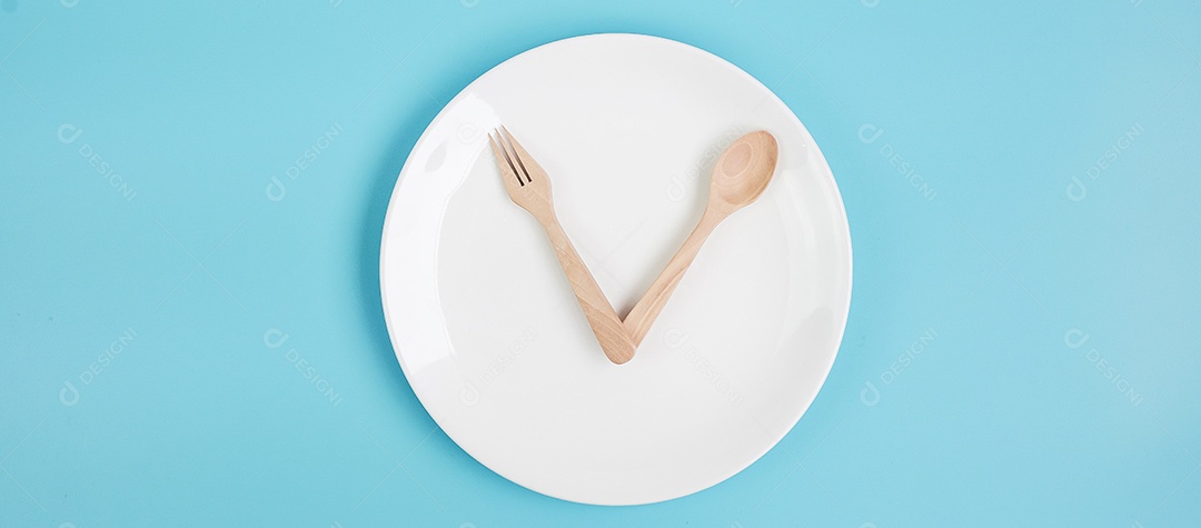 Vista superior placa cerâmica branca com faca, colher e garfo sobre fundo azul. Jejum intermitente, dieta cetogênica, perda de peso