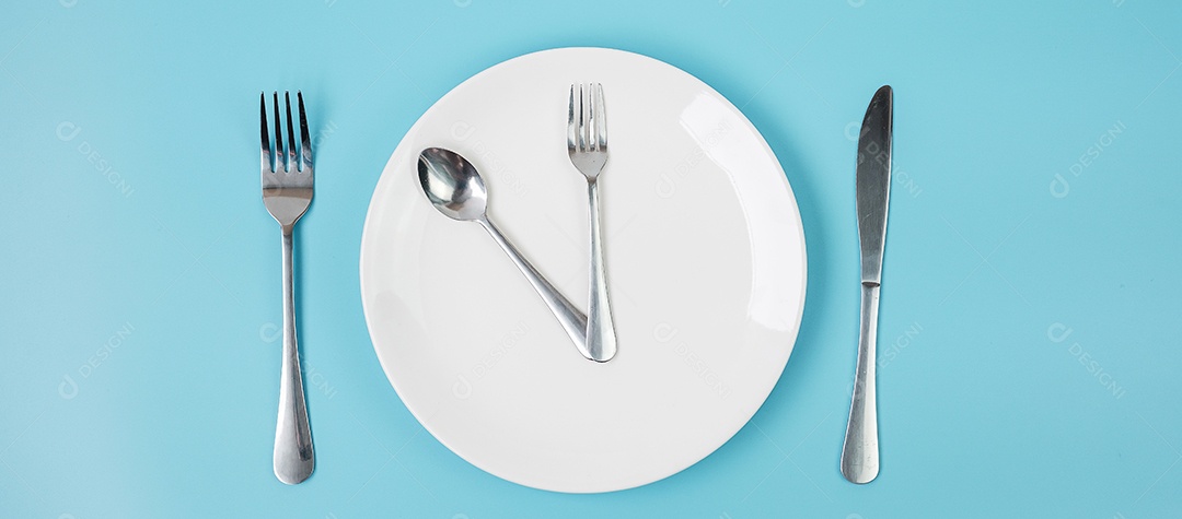 Vista superior placa cerâmica branca com faca, colher e garfo sobre fundo azul. Jejum intermitente, dieta cetogênica, perda de peso