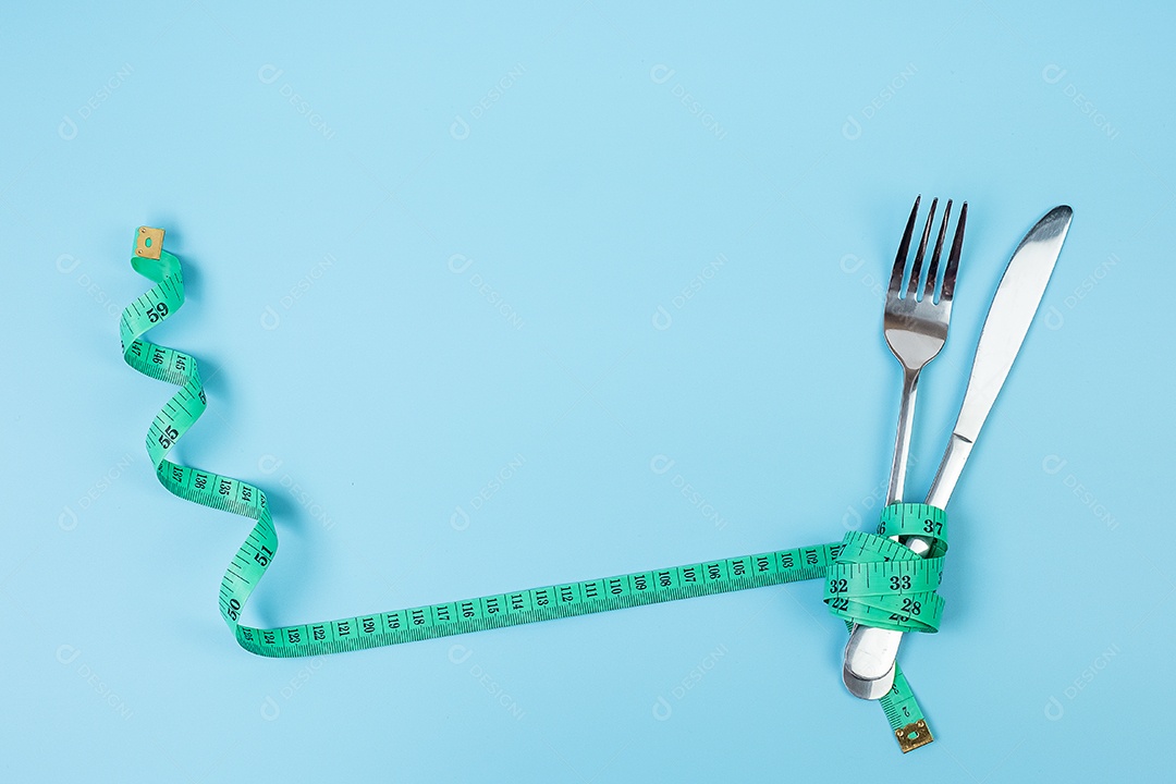 Fita métrica verde enrolada em garfo e faca sobre fundo azul. dieta, perda de peso, obesidade e conceito de controle de alimentos