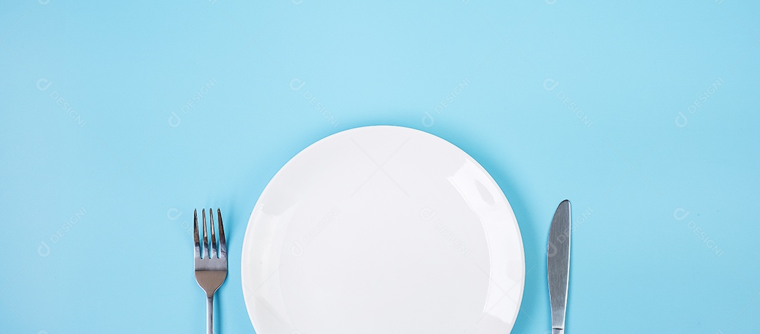 prato de cerâmica branco vazio com faca e garfo sobre fundo azul. conceito de jantar e utensílios de cozinha