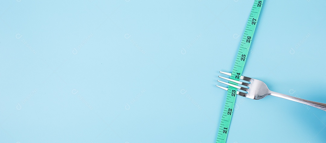 Fita métrica verde enrolada em garfo e faca sobre fundo azul. dieta, perda de peso, obesidade e conceito de controle de alimentos